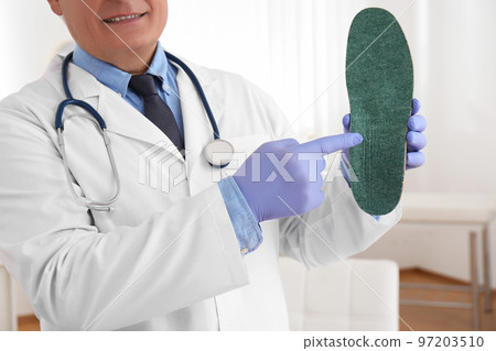 Senior male orthopedist showing insole in clinic, closeup Senior male orthopedist showing insole in clinic, closeup 97203510