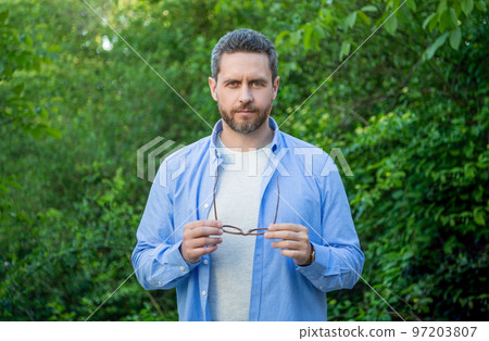 Professional man businessman in blue shirt holding glasses natural background 97203807