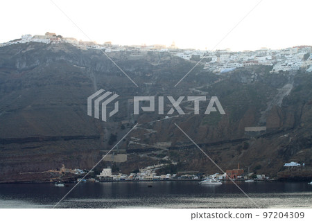 A row of white houses built on Santorini island on the cliffs at dawn 97204309