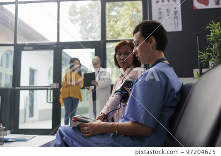 Medical assistant checking hypertension on tonometer in waiting area at health center, measuring blood and pulse pressure. Asian patient doing checkup examination with cardiology test. 97204625
