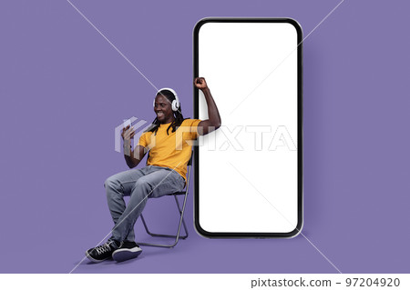Happy black guy watching online video, using wireless headset, smartphone 97204920