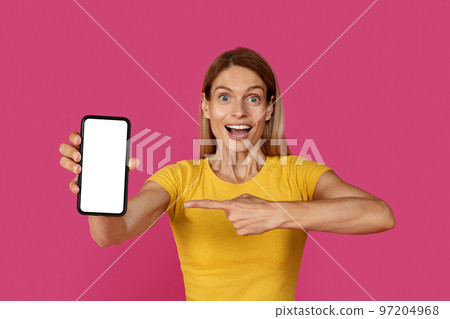Glad surprised inspired mature caucasian blonde woman in yellow t-shirt with open mouth point finger at smartphone Glad surprised inspired mature caucasian blonde woman in yellow t-shirt with open mouth point finger at smartphone 97204968