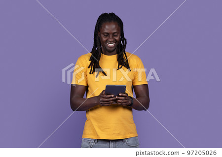 Joyful stylish young black guy using digital tablet on purple Joyful stylish young black guy using digital tablet on purple 97205026