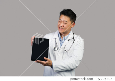 Cheerful mature korean male therapist in white coat with stethoscope shows tablet Cheerful mature korean male therapist in white coat with stethoscope shows tablet 97205202