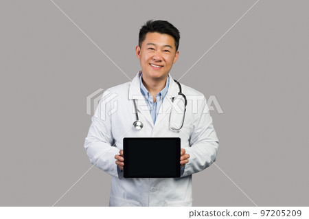 App for health care remote. Smiling korean chinese male therapist in white coat with stethoscope shows tablet 97205209
