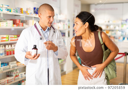 Woman complains to a pharmacist about a sore belly. Help in choosing a medicine in pharmacy Woman complains to a pharmacist about a sore belly. Help in choosing a medicine in pharmacy 97205859