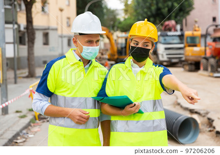 Two engineers in protective masks are discussing a construction plan Two engineers in protective masks are discussing a construction plan 97206206