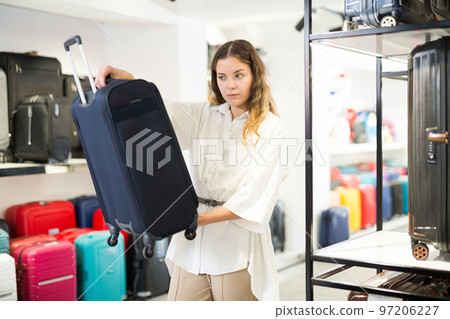 Positive cheerful female customer choosing travel suitcase in shop 97206227