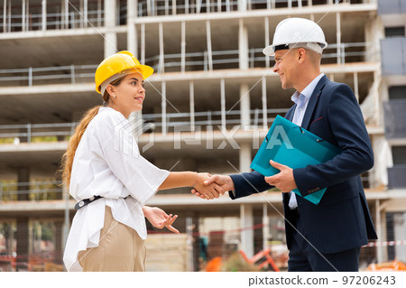Woman client shaking hand with builder at construction site 97206243