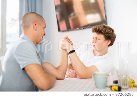 Happy smiling father and son arm wrestling at home Happy smiling father and son arm wrestling at home 97206295