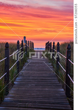 Orange and red sunrise light with straight boardwalk path guiding you to beach Orange and red sunrise light with straight boardwalk path guiding you to beach 97208355