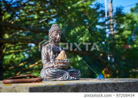 Small Buddhist statue on top of cement column in forest 97208434