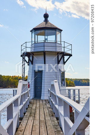 Boardwalk with railing leads to small white lighthouse on Maine river 97208435