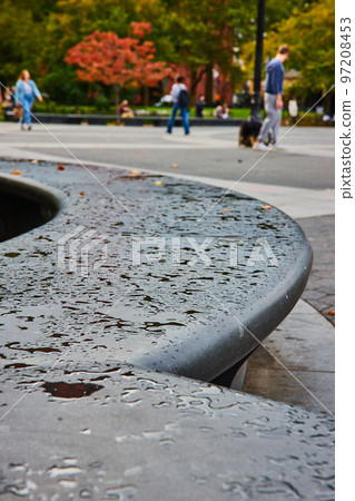 Cement concrete curved seating with patches of water drops and tourists soft in background 97208453