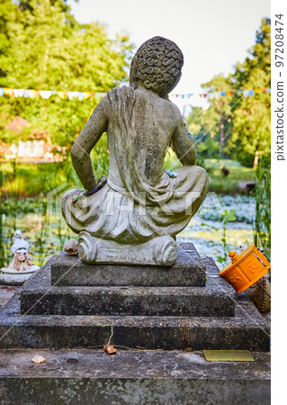 Tibetan Mongolian Buddhist stone statue from behind overlooking lily pond 97208474