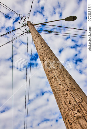 Detail looking up textured wood telephone pole with spotty clouds on blue sky Detail looking up textured wood telephone pole with spotty clouds on blue sky 97208584