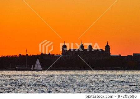 Silhouette of Ellis Island with boat sailing past and intense orange sky 97208690