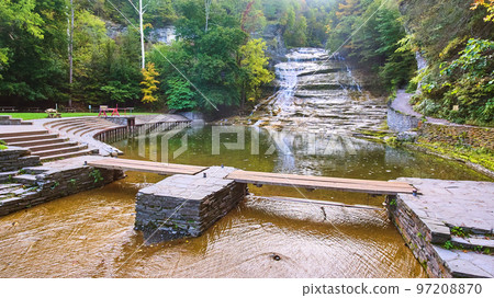 Huge waterfall terracing down into river with walking bridge and seating area 97208870