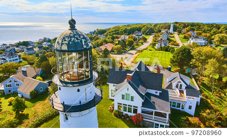 Up close aerial at top of white lighthouse with homes and ocean view in Maine 97208960
