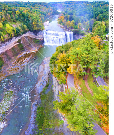 Aerial panorama over road along edge of cliffs with raging waterfall and bridge in background 97209019
