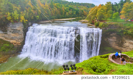 Huge raging waterfall in river through canyon with colorful foliage and tourists admiring from vista 97209021