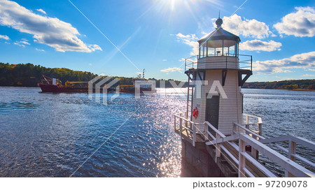 Large commercial ship on Maine river sails past small lighthouse with blue skies 97209078