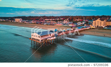 Serene morning light over old pier covered in shop from drone over ocean with view of beach and town Serene morning light over old pier covered in shop from drone over ocean with view of beach and town 97209106