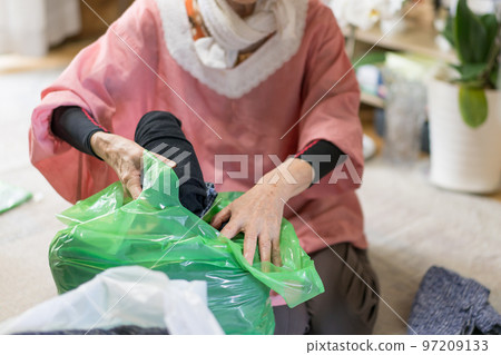 A senior woman disposing of unwanted clothes by putting them in garbage bags Sorting out belongings A senior woman disposing of unwanted clothes by putting them in garbage bags Sorting out belongings 97209133