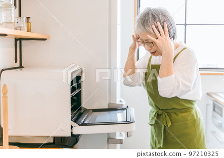 Asian elderly woman using microwave oven to cook food in home kitchen (confused) 97210325