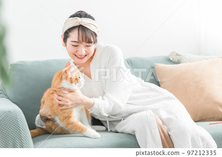 亞洲女主人在家裡的沙發上抱著一隻貓 97212335