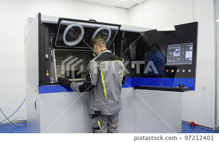 A worker looks into open window of inside large industrial 3D printer for metal powder. The working process. Industrial powder 3d printer for metal and worker man. Laser sintering machine for metal. A worker looks into open window of inside large industrial 3D printer for metal powder. The working process. Industrial powder 3d printer for metal and worker man. Laser sintering machine for metal. 97212401
