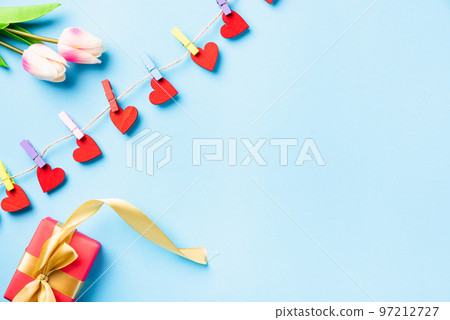Happy Valentine's day concept. red heart-shaped valentines decoration hanging with clips for love and red gift box with golden ribbon on the rope greeting card on blue background with copy space Happy Valentine's day concept. red heart-shaped valentines decoration hanging with clips for love and red gift box with golden ribbon on the rope greeting card on blue background with copy space 97212727
