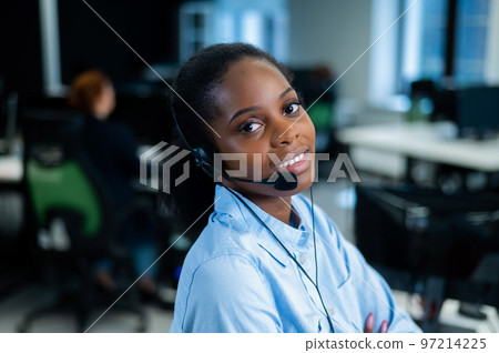 African young woman talking to a client on a headset. Female employee of the call center. 97214225
