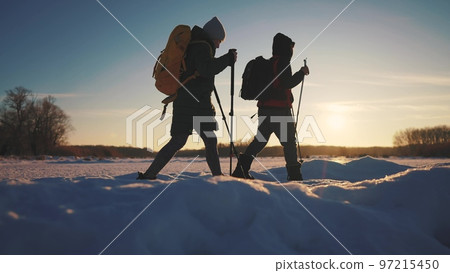 nordic walking in winter. winter hike group of tourists silhouette. teamwork travel. two hikers with sticks walk in the winter sunset in the snow at silhouette. activities in winter happy family nordic walking in winter. winter hike group of tourists silhouette. teamwork travel. two hikers with sticks walk in the winter sunset in the snow at silhouette. activities in winter happy family 97215450