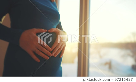 woman pregnant. motherhood sunset a pregnancy concept. 40 year old pregnant woman stands in a dress by the window holding her stomach silhouette. silhouette of a girl in by the window woman pregnant. motherhood sunset a pregnancy concept. 40 year old pregnant woman stands in a dress by the window holding her stomach silhouette. silhouette of a girl in by the window 97215457
