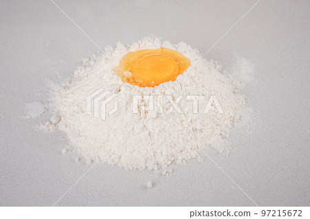 Egg yolk in the nest of flour on a white background in a horizontal position. Dough kneading Egg yolk in the nest of flour on a white background in a horizontal position. Dough kneading 97215672