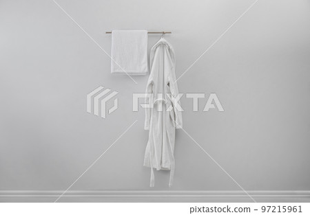 Rack with clean bathrobe and towel on light wall 97215961