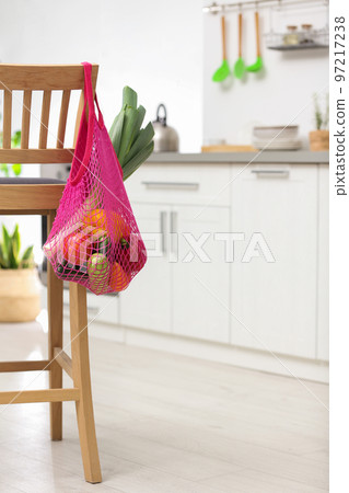 Net bag with vegetables hanging on wooden chair in kitchen Net bag with vegetables hanging on wooden chair in kitchen 97217238