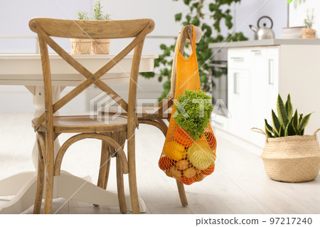 Net bag with vegetables hanging on wooden chair in kitchen Net bag with vegetables hanging on wooden chair in kitchen 97217240