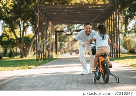 Dad and a gitl looking happy spending time in the park and riding a bike Dad and a gitl looking happy spending time in the park and riding a bike 97219247