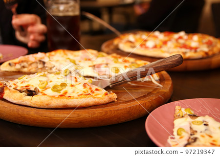Defocus background of italian pizza with green olives standing in table. Tortilla with grated Mozzarella. Pizza with olives, Basil and cheese close up. Pizzeria outside. Out of focus Defocus background of italian pizza with green olives standing in table. Tortilla with grated Mozzarella. Pizza with olives, Basil and cheese close up. Pizzeria outside. Out of focus 97219347