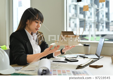 Beautiful architects woman working on design of a construction plan and scale model house at office Beautiful architects woman working on design of a construction plan and scale model house at office 97219545