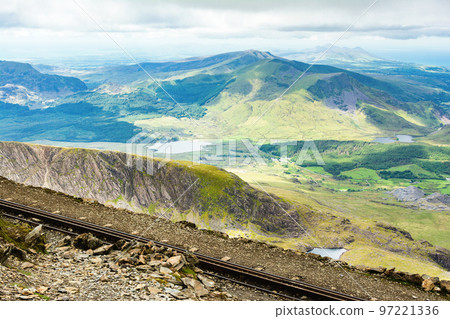 Climbing up mount Snowdon in North Wales. View of the hills and mountains, green grass and beautiful blue lakes on the way to the top. 97221336
