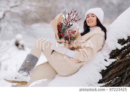 A girl in a beige cardigan and winter flowers walks in nature in the snowy season. Winter weather A girl in a beige cardigan and winter flowers walks in nature in the snowy season. Winter weather 97223425