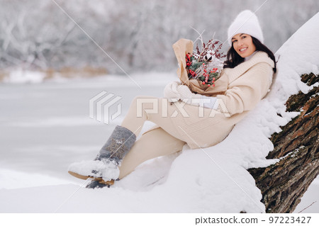 A girl in a beige cardigan and winter flowers walks in nature in the snowy season. Winter weather A girl in a beige cardigan and winter flowers walks in nature in the snowy season. Winter weather 97223427