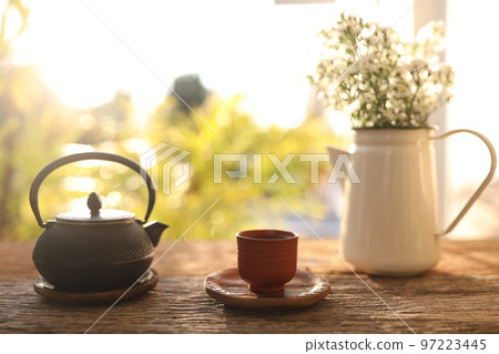 Tea cup and black metal tea pot and flowers on wooden table Tea cup and black metal tea pot and flowers on wooden table 97223445