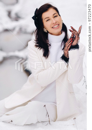 Portrait of a stylish woman in a white suit with elegant gloves sitting in nature in winter Portrait of a stylish woman in a white suit with elegant gloves sitting in nature in winter 97223470