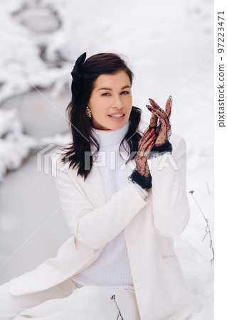 Portrait of a stylish woman in a white suit with elegant gloves sitting in nature in winter 97223471