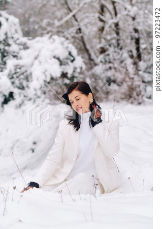 Portrait of a stylish woman in a white suit with elegant gloves sitting in nature in winter 97223472