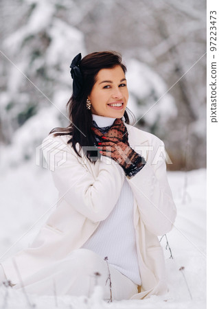 Portrait of a stylish woman in a white suit with elegant gloves sitting in nature in winter 97223473